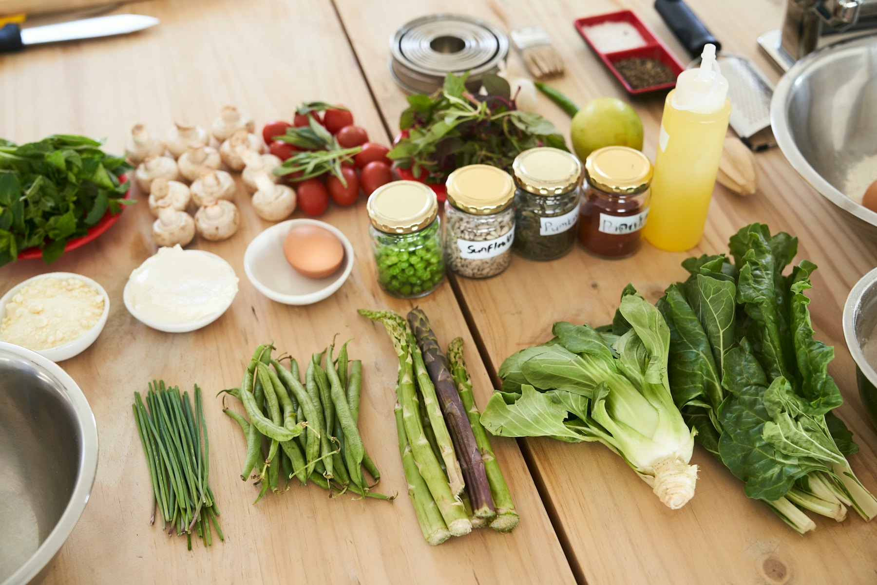 Fresh vegetables, herbs, an egg, and labeled jars of ingredients laid out on a wooden table